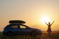 Dark silhouette of woman driver standing near her car on grassy field enjoying view of bright sunset. Young female Royalty Free Stock Photo