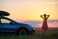 Dark silhouette of woman driver standing near her car on grassy field enjoying view of bright sunset. Young female Royalty Free Stock Photo