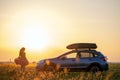 Dark silhouette of woman driver standing near her car on grassy field enjoying view of bright sunset. Young female Royalty Free Stock Photo