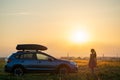 Dark silhouette of woman driver standing near her car on grassy field enjoying view of bright sunset. Young female Royalty Free Stock Photo