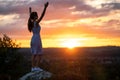 Dark silhouette of a young woman standing with raised up hands on a stone enjoying sunset view outdoors in summer Royalty Free Stock Photo