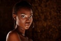 Dark skinned beautiful young woman posing sensually on a golden background. Royalty Free Stock Photo