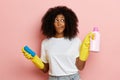 Dark skinned curly haired housewife looks to the right while cleaning, she holds a brush and cleaning liquid