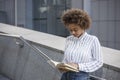 The dark-skinned girl is standing on the steps leaning on the railing. She is reading a book in the street near the office