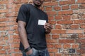 Dark-skinned man in T-shirt showing blank business card on bricked background. Royalty Free Stock Photo