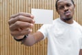 Dark-skinned man in white T-shirt showing blank business card to camera. Royalty Free Stock Photo