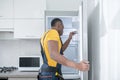 Dark-skinned service man in yellow tshirt standing near the fridge