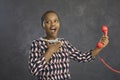 Dark-skinned shocked woman holding red retro telephone handset with wire on gray background. Royalty Free Stock Photo