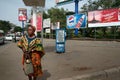 Dark-skinned Tanzanian woman stands on street surrounded by outdoor advertising.