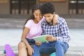 Dark-skinned teens watching video on digital tablet sitting outdoors