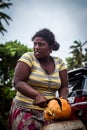 A dark-skinned woman cuts an orange coconut with a big knife. Working hard women. Strong and worthy woman doing hard job