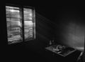 Dark small room in old apartment with wooden table and chairs near the window, sunlight coming through the blinds.