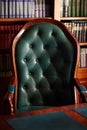 Dark solid interior of old library with books on the wooden shelves. Vintage classic chair green leather and red wood, antique tab