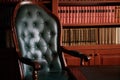 Dark solid interior of old library with books on the wooden shelves. Vintage classic chair green leather and red wood, antique tab Royalty Free Stock Photo