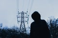 A dark spooky, moody edit. A hooded figure looking at the camera below an energy electricity pylon on a winters evening in the Royalty Free Stock Photo