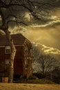 Dark spooky two story brick house with stark winter tree overhanging under ominous sky and strange late day light