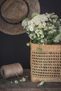 Dark still life scene with a bunch of wild flowers in a basket and a hat on a wall Royalty Free Stock Photo