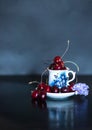 Dark stillife with porcelain cup of fresh cherries with purple flower