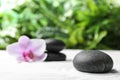 Dark stones and beautiful flower on sand against green background. Zen, meditation, harmony Royalty Free Stock Photo