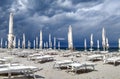 Dark and stormy sky, with gray clouds on the blue sea and a little beach with deck chairs and closed white umbrellas in the Royalty Free Stock Photo