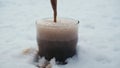 Dark, strong stout beer is poured into a glass standing in the snow