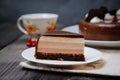 On a dark tabletop on a linen napkin, a tea composition: on a saucer a piece of cake made of three chocolate layers of different Royalty Free Stock Photo