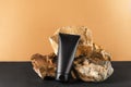 Dark tube with soft moisturizing lotion for body. Blank unbranded flacon for mans skincare. Stone on golden and black background.