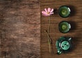 Dark turquoise glazed clay teapot and small cups on dark wooden background with bamboo mat decorated with pink flower. Flat lay
