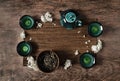 Dark turquoise glazed clay teapot and small cups on dark wooden background with bamboo mat decorated with white flowers. Flat lay