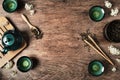 Dark turquoise glazed clay teapot and small cups on dark wooden background decorated with white flowers. Flat lay style