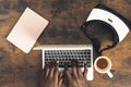 Dark wood working desk man writing on computer laptop with notebook VR headset and coffe cup - overtop shot