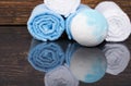 On a dark wooden background with reflection, blue bath salt in the form of a relaxation bomb and towels wrapped in a roll