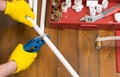 On a dark wooden background and tools, the hands of a worker in yellow gloves, scissor a white plumbing pipe