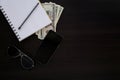 Dark wooden desk with objects. Top view of a notebook, money, cell, phone, pen and sunglasses Royalty Free Stock Photo