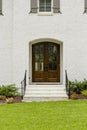 Dark wooden front door with a small arch and black rails with green grass