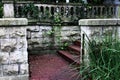 Darkly weather stained deeply eroded cement wall surrounding brick steps