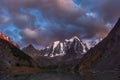 Darkness mountain landscape with great snowy mountain lit by dawn sun among dark clouds. Awesome alpine scenery with high mountain