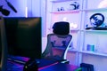 Darkroom for a professional gamer with a comfortable empty gamer chair, computer table, neon lights, keyboard, monitor,