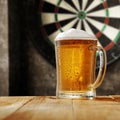 Dartboard with grey wall background. A big glass of cold beer on wooden table with empty space. Darts playing time. Royalty Free Stock Photo