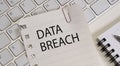 Data Breach text on paper lying on the keyboard with a notepad and a pen.