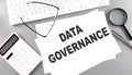 DATA GOVERNANCE text on paper with keyboard, calculator on grey background