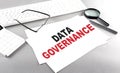 DATA GOVERNANCE text on a paper with keyboard, calculator on grey background