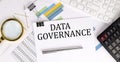 DATA GOVERNANCE text on the white paper on the light background with charts paper ,keyboard and calculator