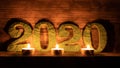 date two thousand twenty stand on a shelf, against the background of wooden boards lit by the light of burning candles.