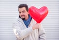 Dating, romance and love concept: happy man showing from behind of heart-shaped red air balloon with funny smiling face