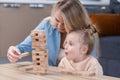 daugher looking excited to Jenga wooden bricks tower, mother teaching cute girl to play board games