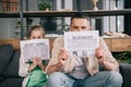 Daughter and father covering faces with business and sport news newspapers