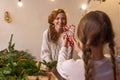 Daughter gives heart-shaped candy canes to mother in workshop interior. DIY Christmas wreath