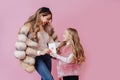 Daughter gives her mother a card with a heart, they are dressed in fur coats