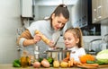 Daughter helping cooking soup and mother add pepper to pan Royalty Free Stock Photo